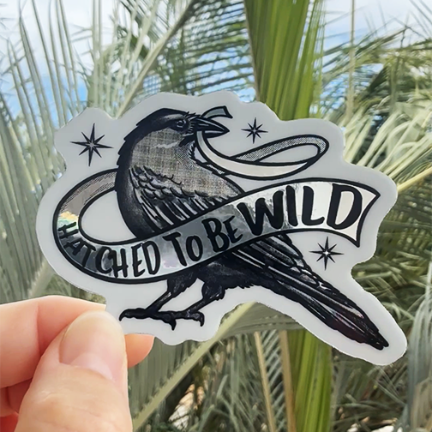 Metallic sticker with an 'alalā (alala) Hawaiian crow design holding a banner that reads, 'Hatched to be Wild.' 